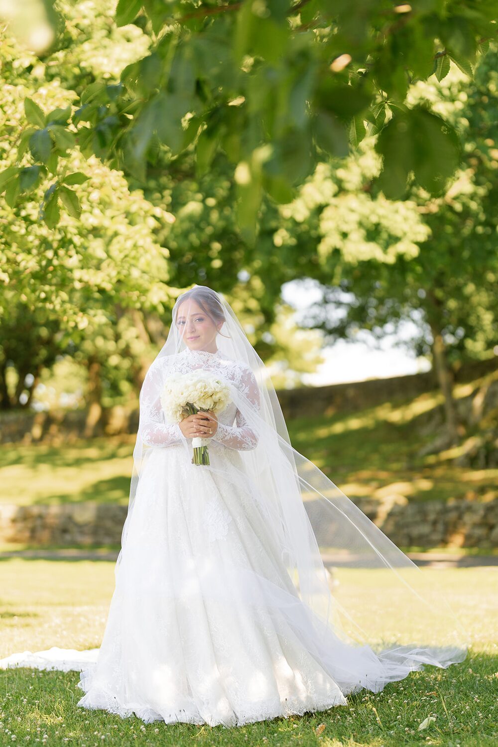 The bride holds her bouquet in a soft veil portrait on the summer lawn.