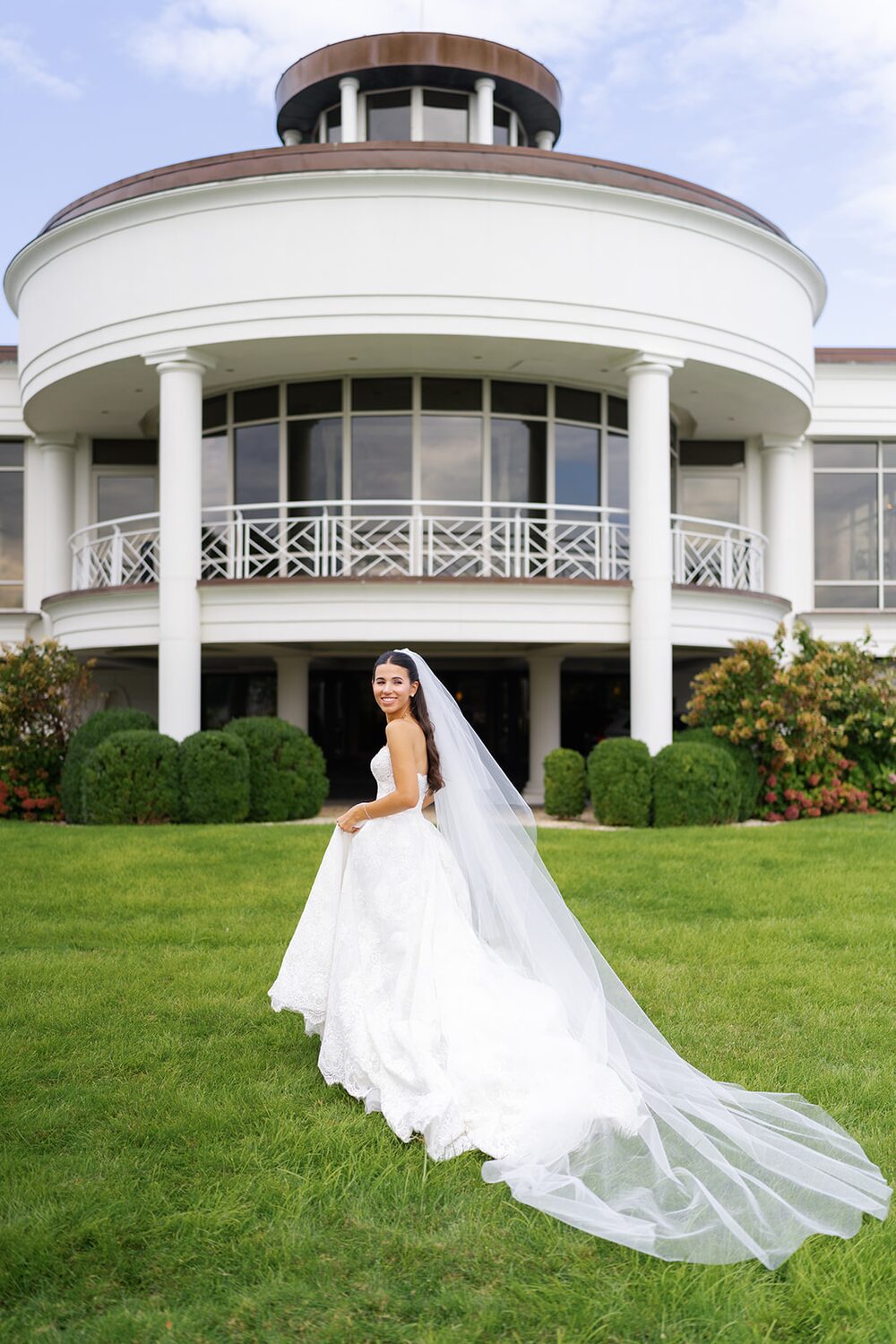 The bride poses alone on the lawn, her long veil trailing before the rotunda facade.