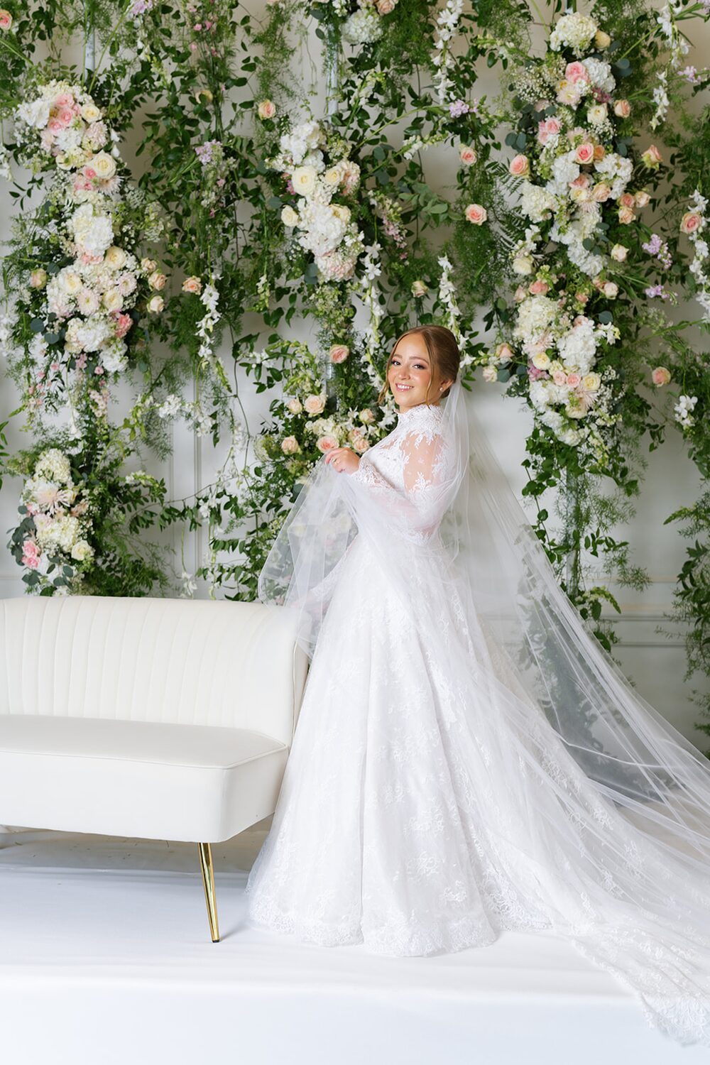 The bride reclines on a white sofa before a lush floral installation.