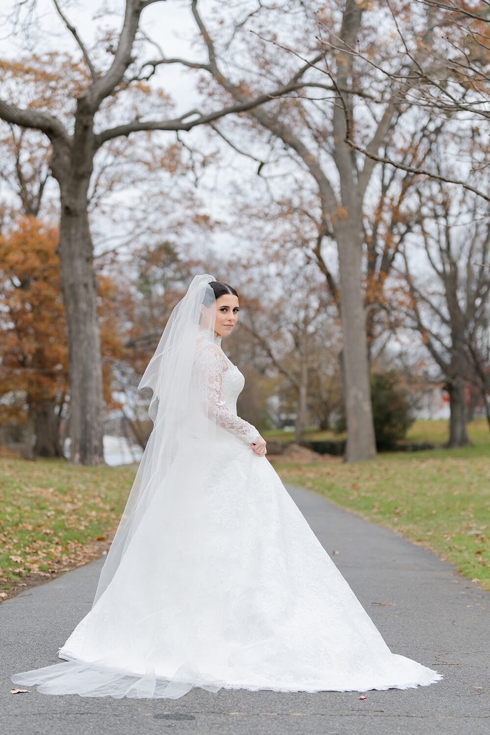 The bride gathers her train on a November park path in Westchester.