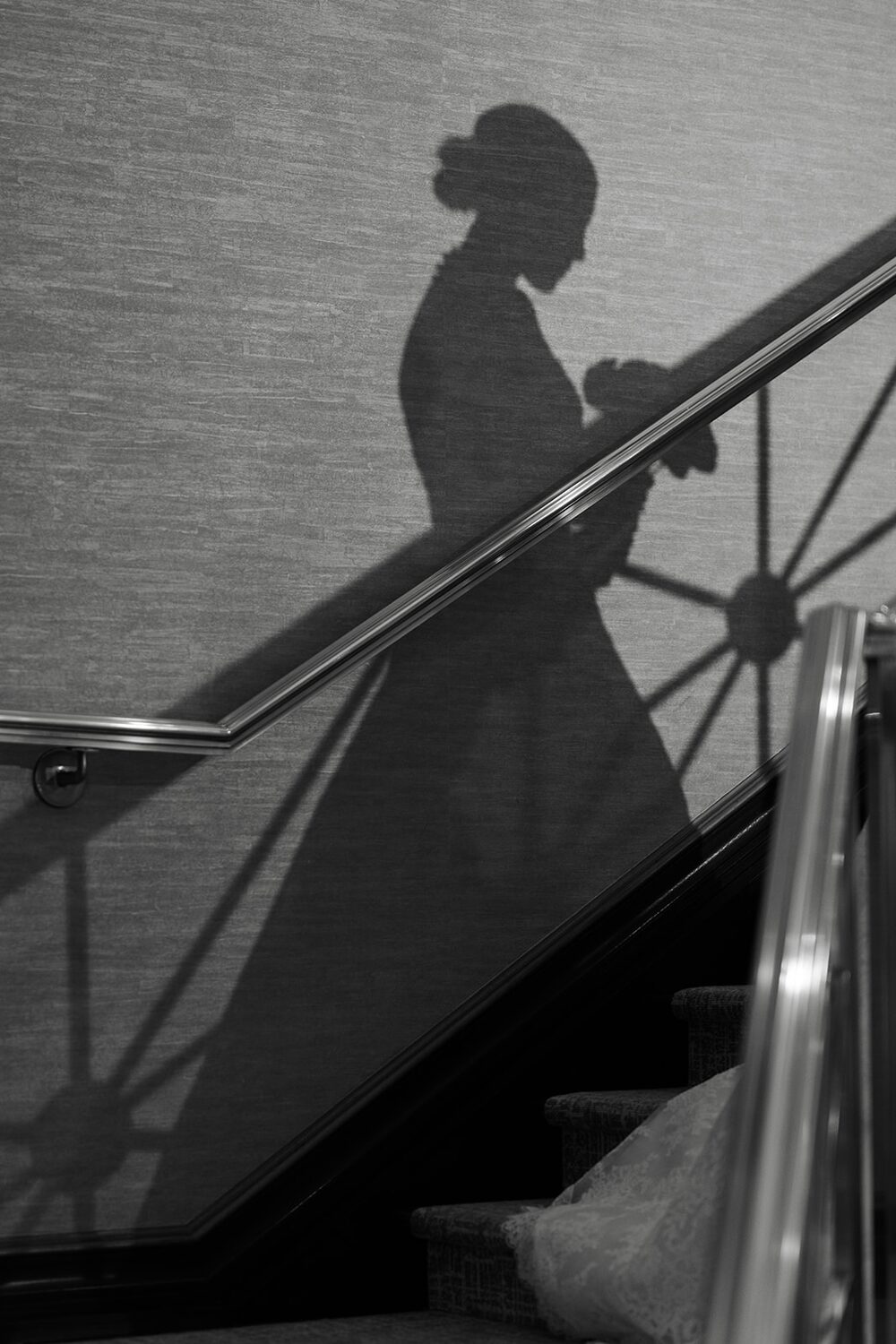 The bride's silhouette falls across the staircase wall in a graphic black and white frame.