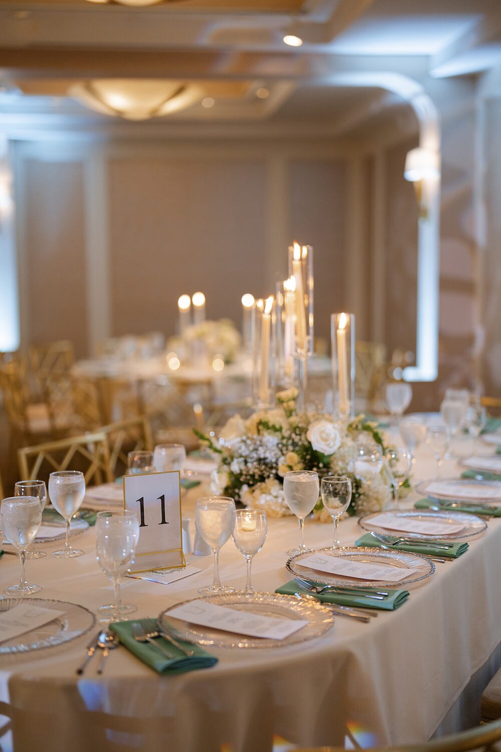 A candlelit reception table set with white florals and sage green napkins in the ballroom.