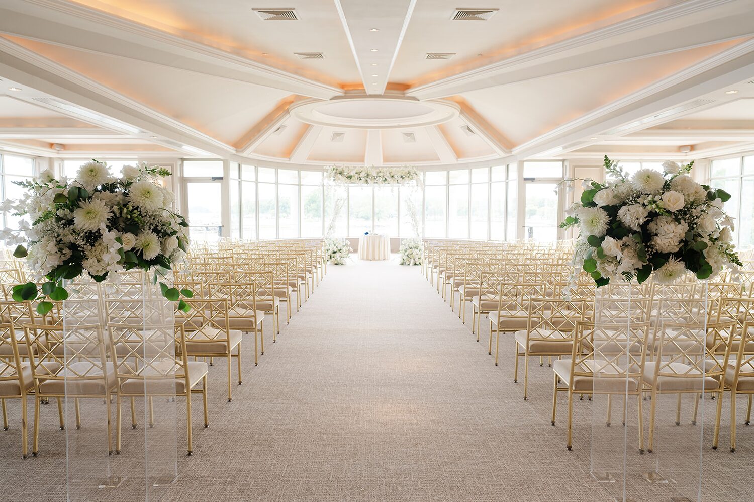 The ceremony aisle waits, lined with white florals on lucite stands and gold chairs.