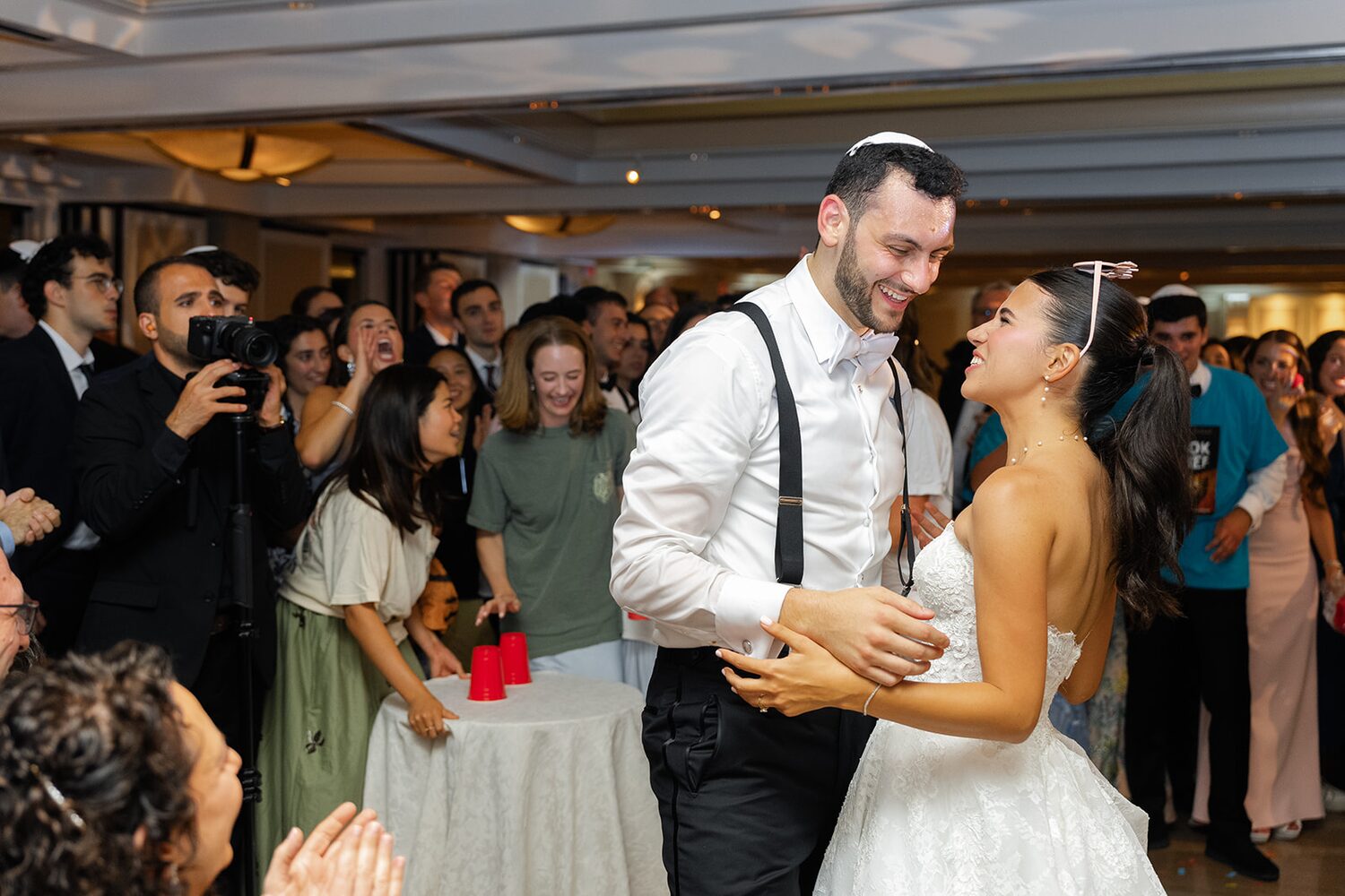 The groom in suspenders dances with his bride in the middle of a packed dance floor.