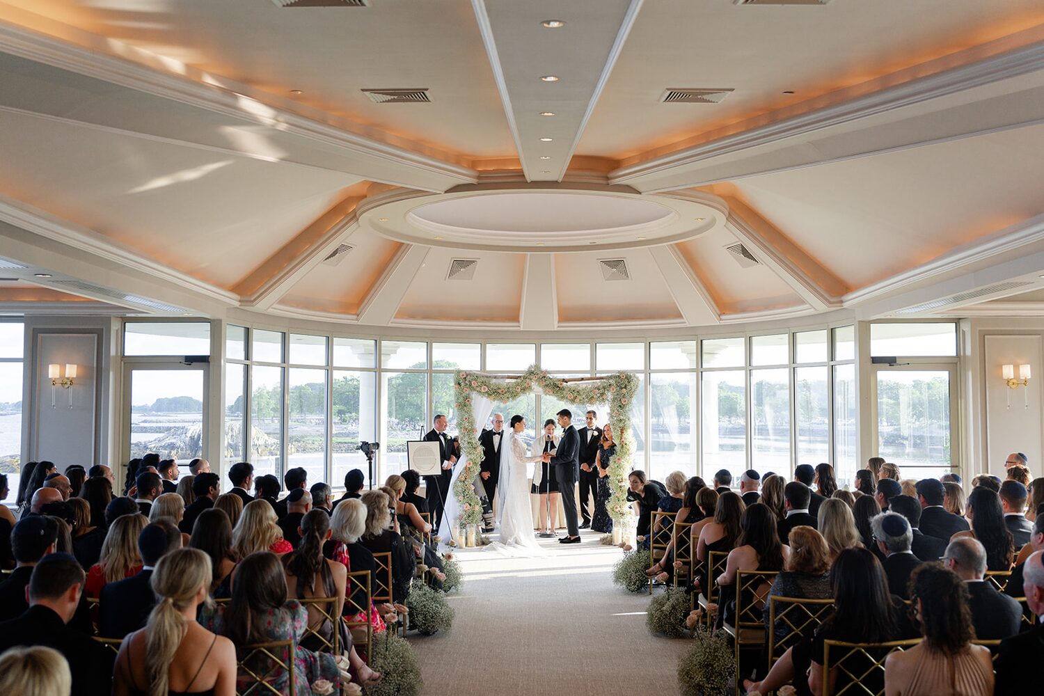 The full ceremony under the domed ceiling, panoramic windows opening to the water.