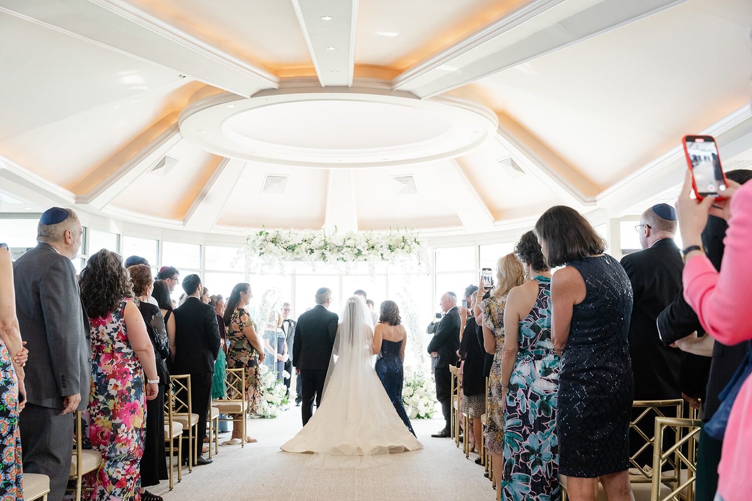The bride's father walks her down the aisle as guests stand on both sides.