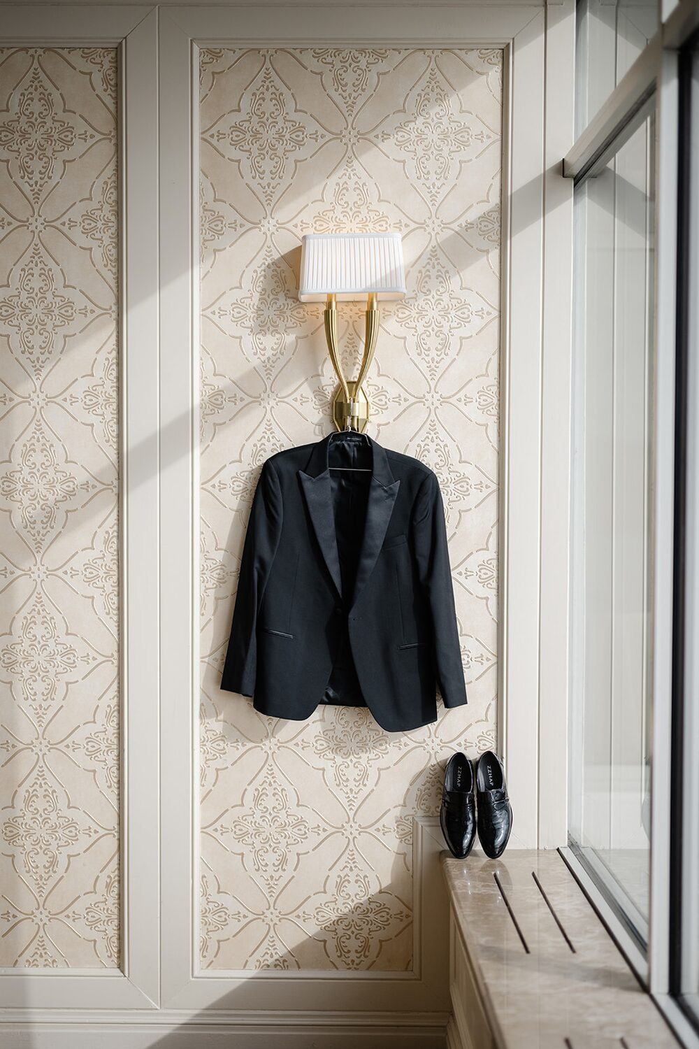 The groom's tuxedo jacket and patent shoes hang beside a glowing sconce before the day begins.