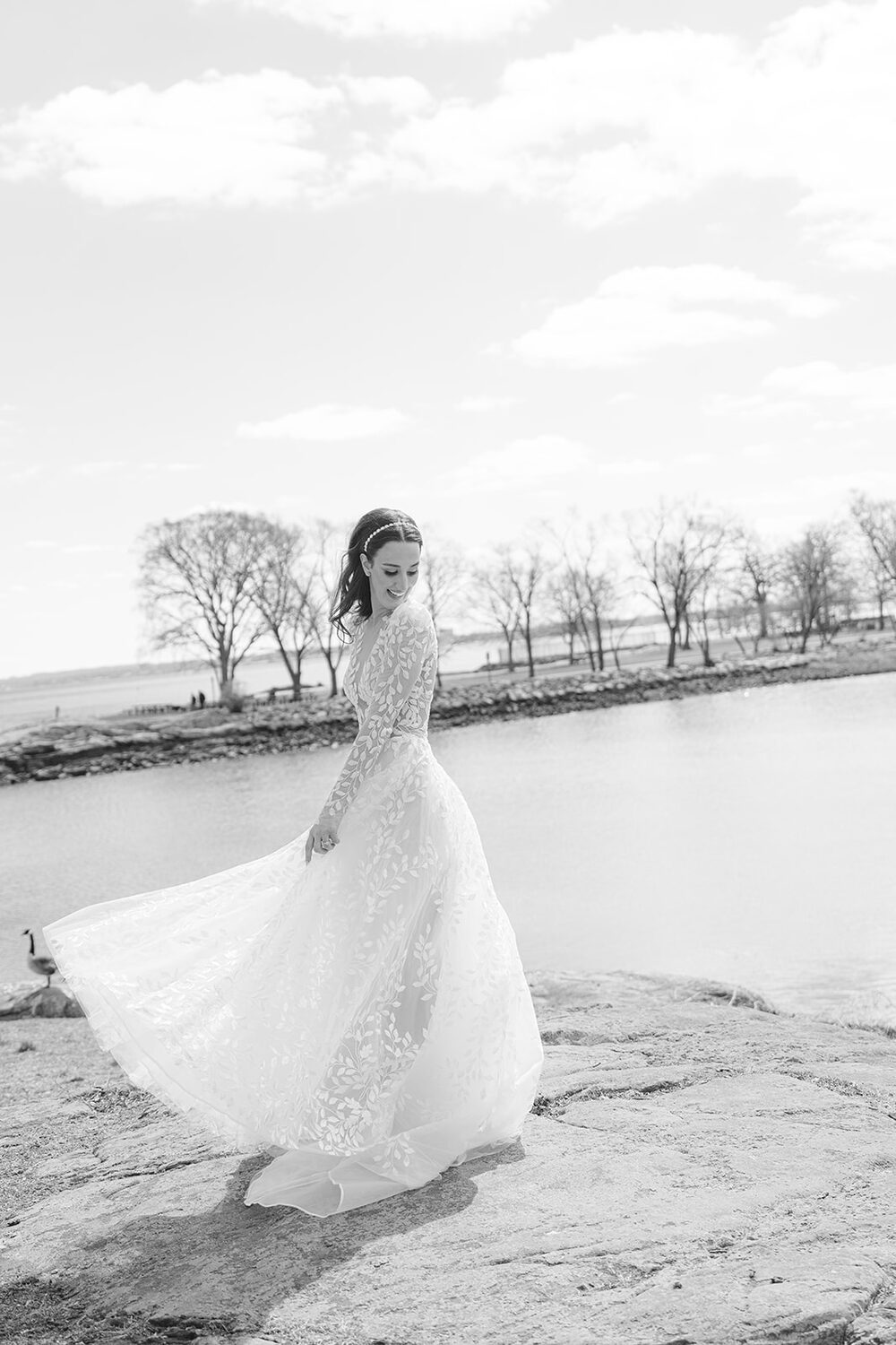 A high-key black and white frame of the bride twirling her gown on the rocks.