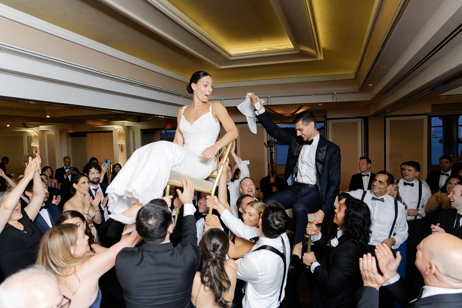 The bride rises on a chair, handkerchief in hand, as the hora swirls below.