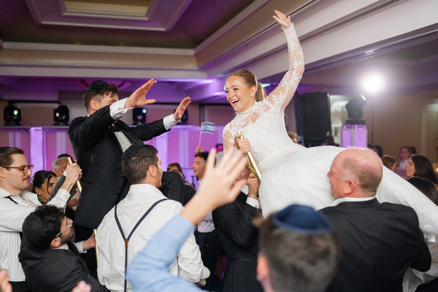 The bride is lifted high on a chair during the hora as the crowd dances below.