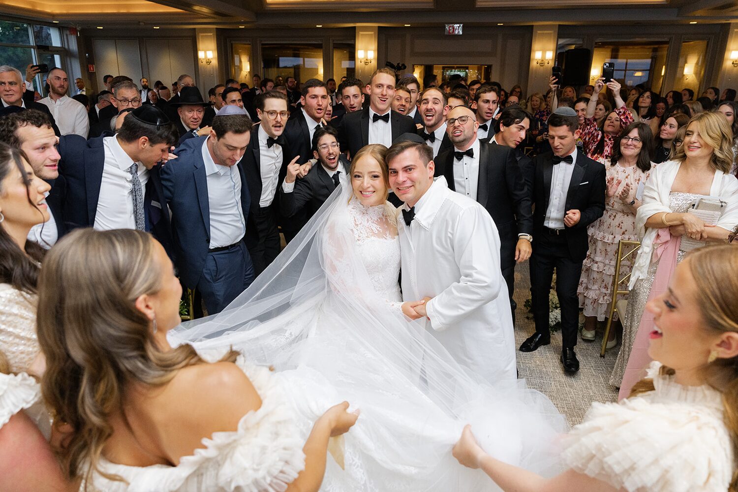 Friends and family surround the bride at the kabbalat panim, her veil spread wide.