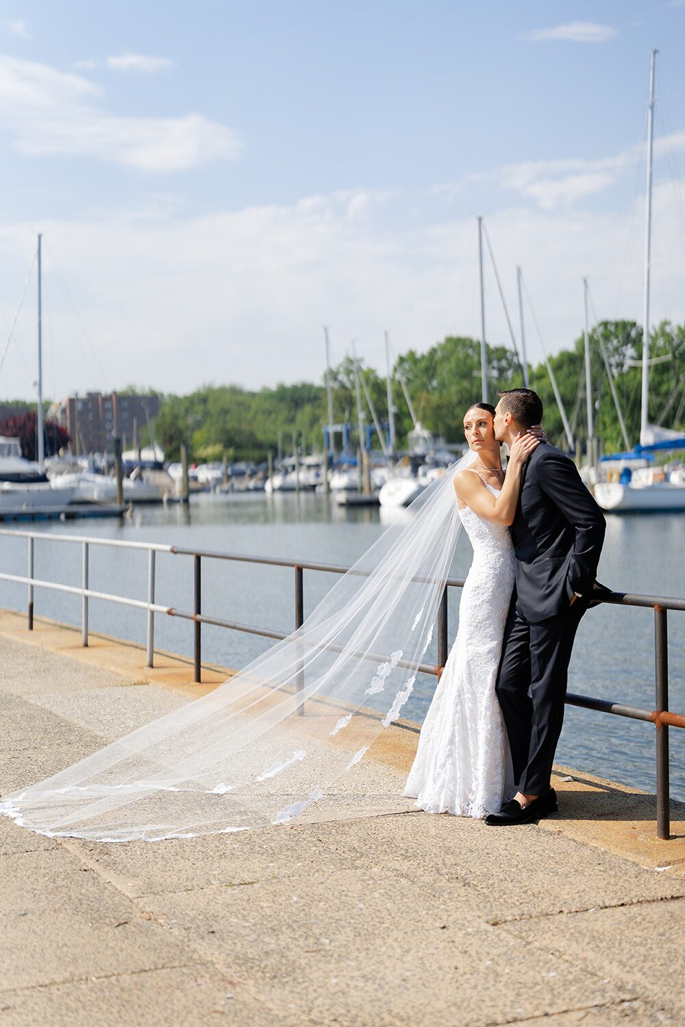 A kiss on the marina boardwalk, sailboat masts rising behind them.