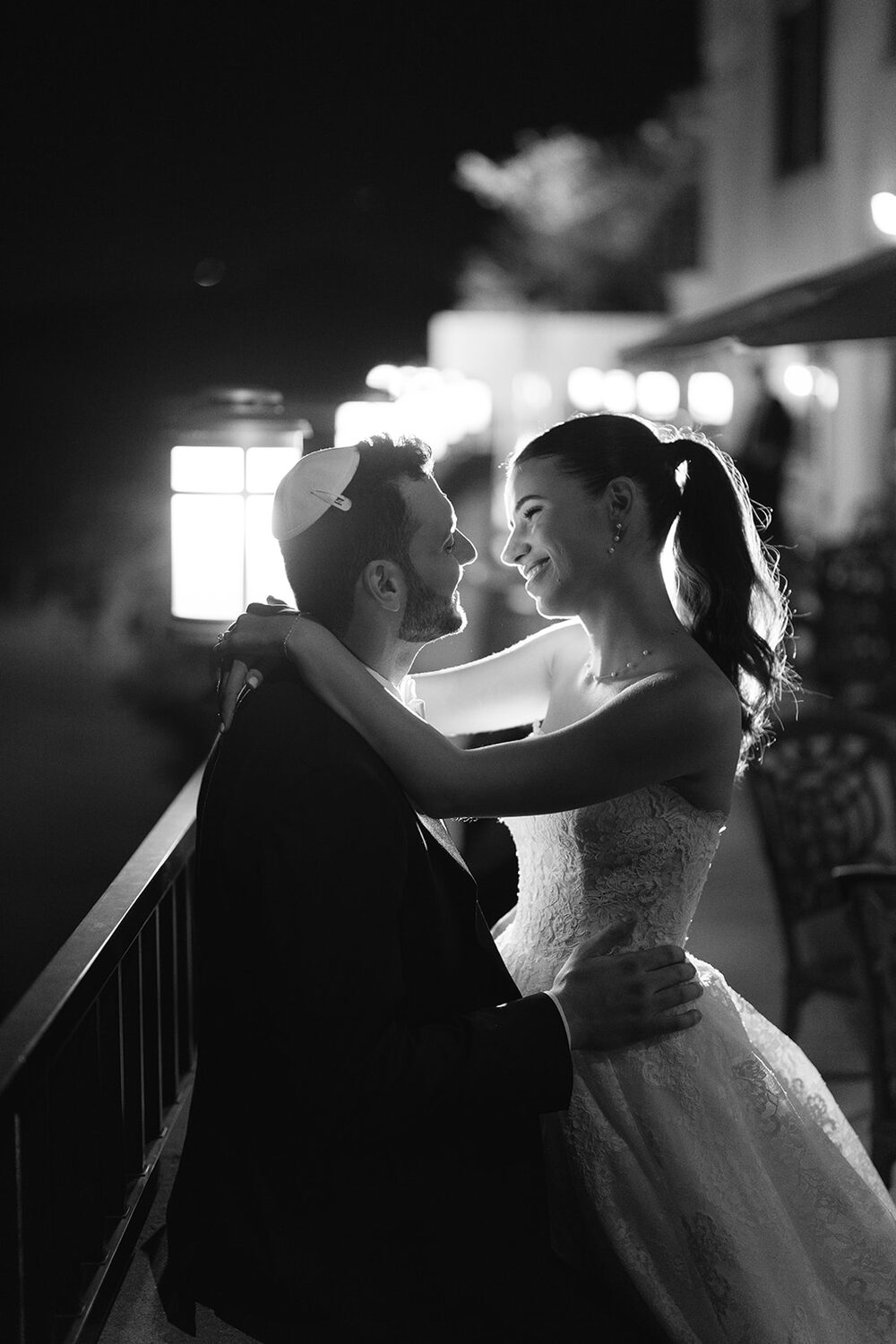 The newlyweds share a quiet embrace on the balcony at night, lit by a single lantern.