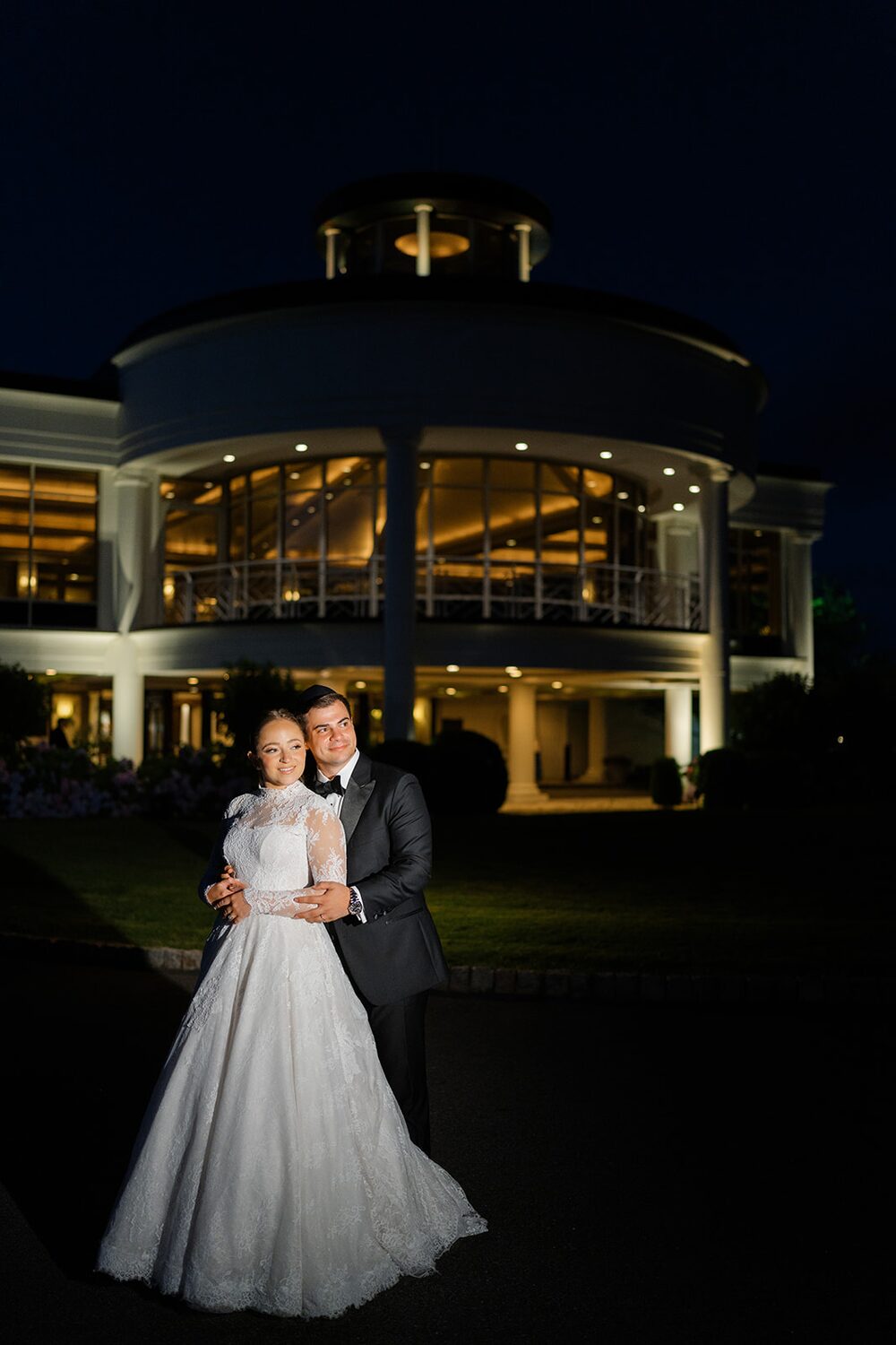 The couple poses at night before the warmly illuminated rotunda of Glen Island Harbour Club.
