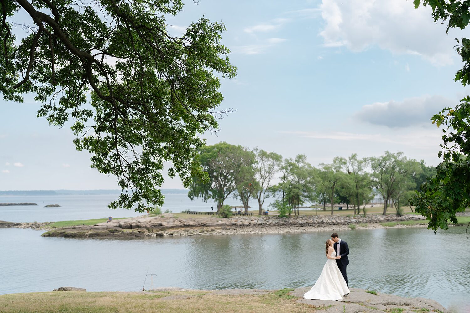 The couple stands at the pond cove near the boat lookout, water still as glass.