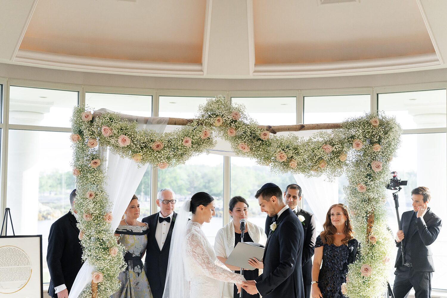Rachel and Daniel exchange private vows beneath the rose-garland chuppah with their parents beside them.