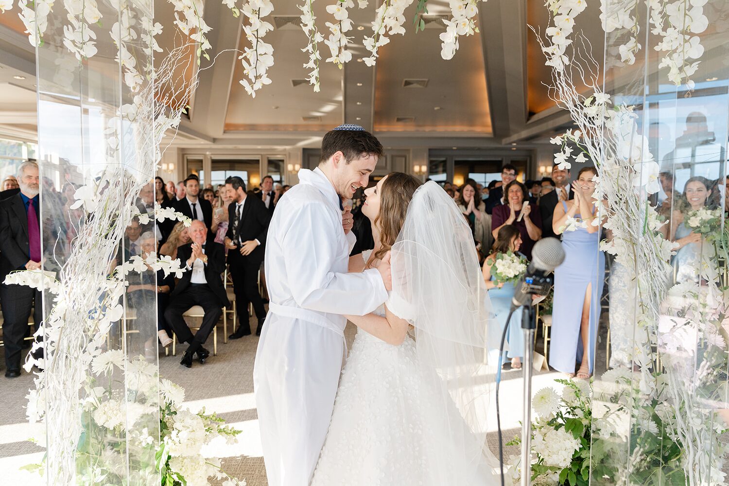 Rebecca and Maor celebrate at the tisch, white orchid branches framing the moment.