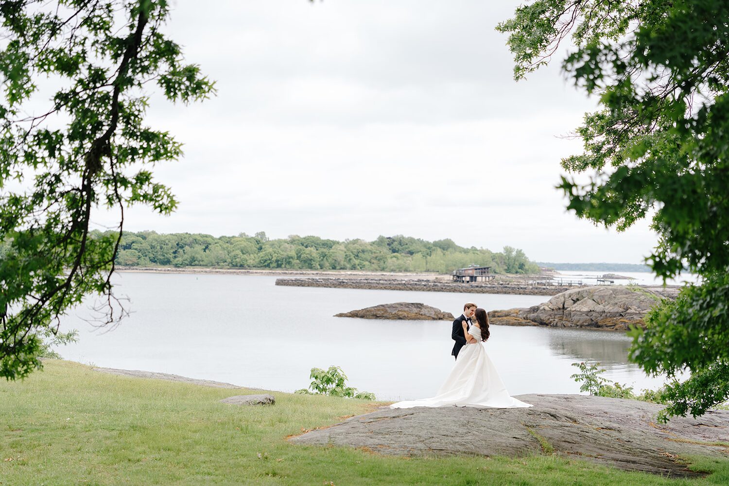 Bride and groom stand together on the rocky cove shoreline of the island.