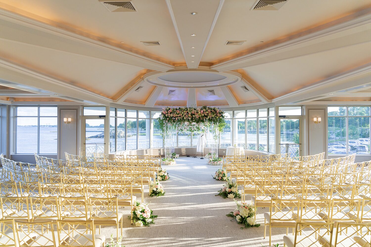 A suspended floral chuppah floats above the aisle in the glass ceremony room before guests arrive.