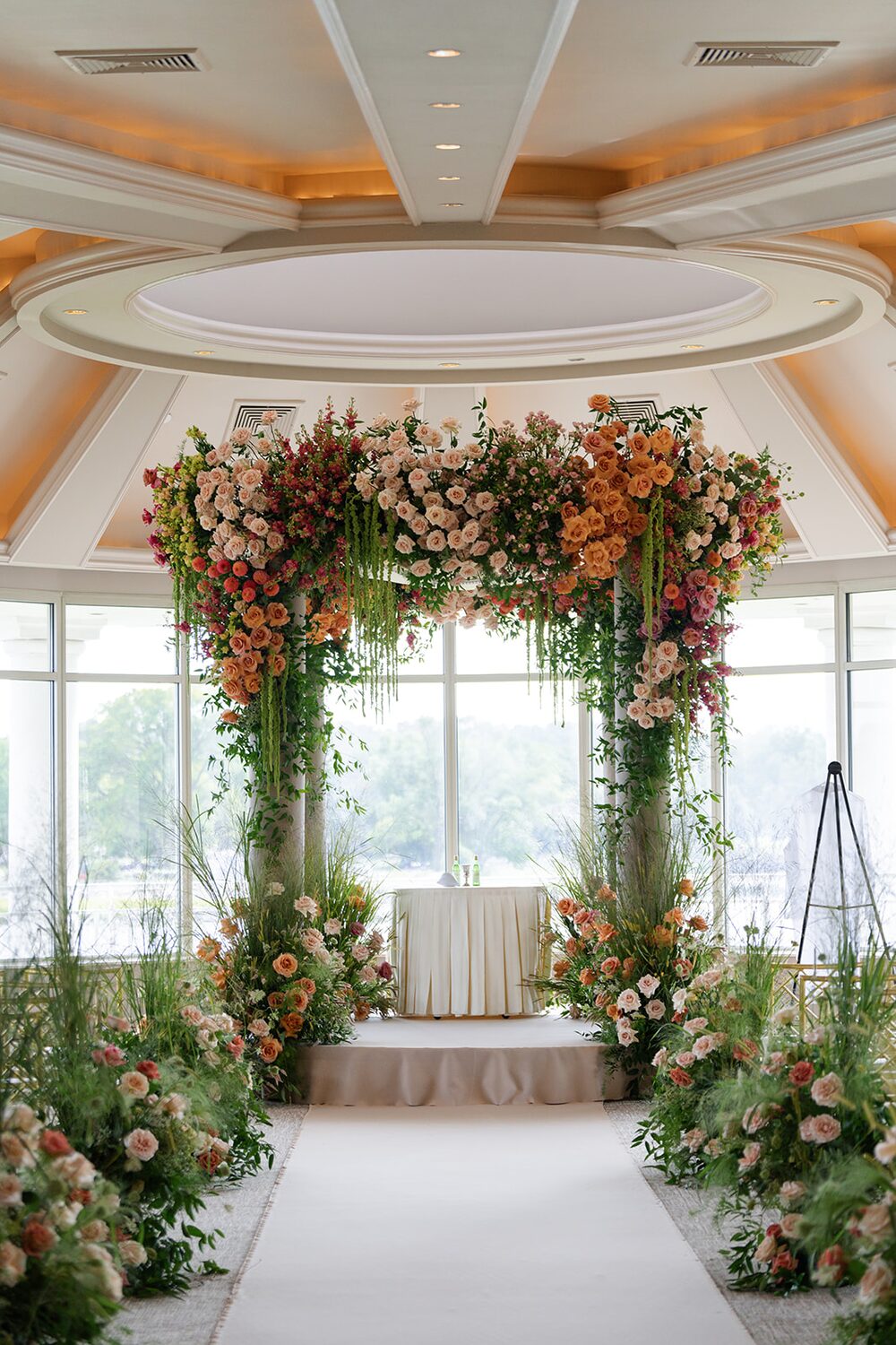 A chuppah of terracotta and mauve roses stands in the glass rotunda before the ceremony.