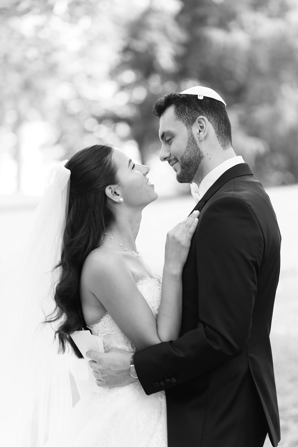 Forehead to forehead beneath her veil, the couple pauses outdoors in black and white.