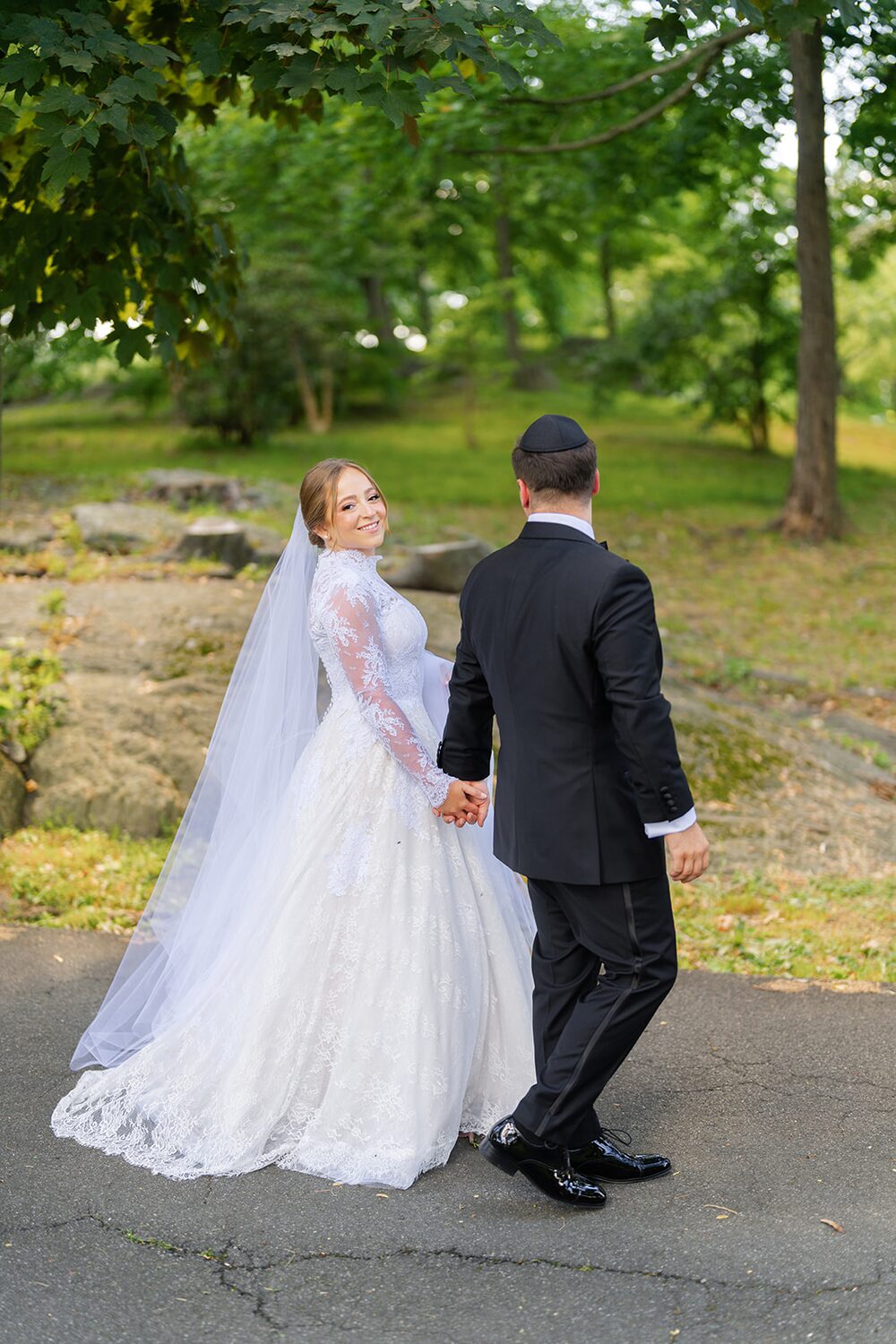 Hand in hand, bride and groom walk away down a wooded path in Westchester.