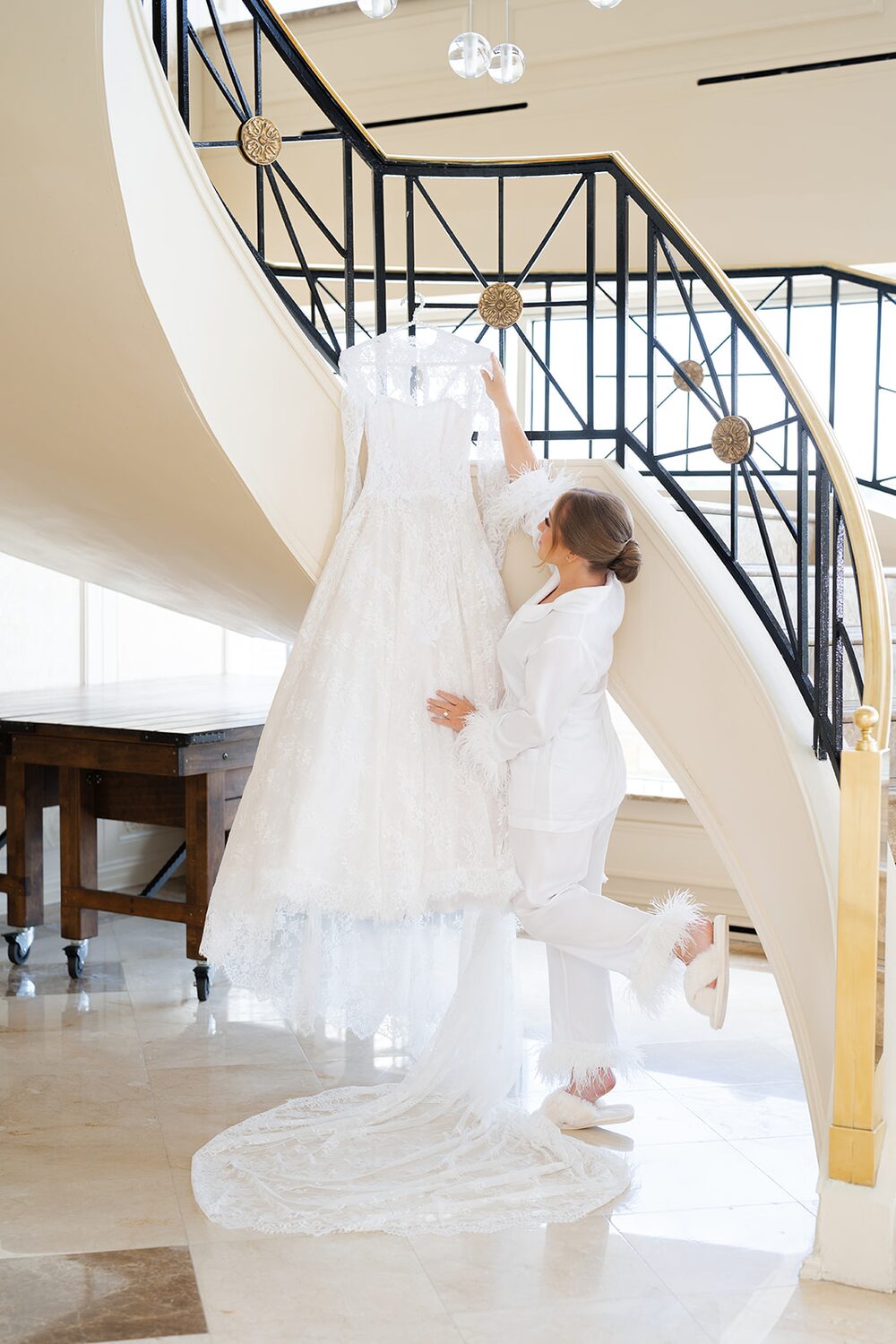 The bride lifts her gown from the spiral staircase in the mansion's marble foyer.