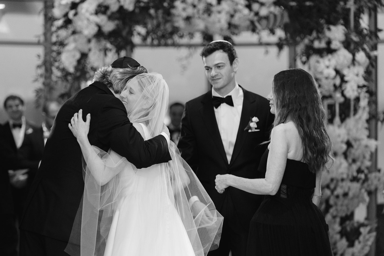 Black and white of family hugs under the chuppah