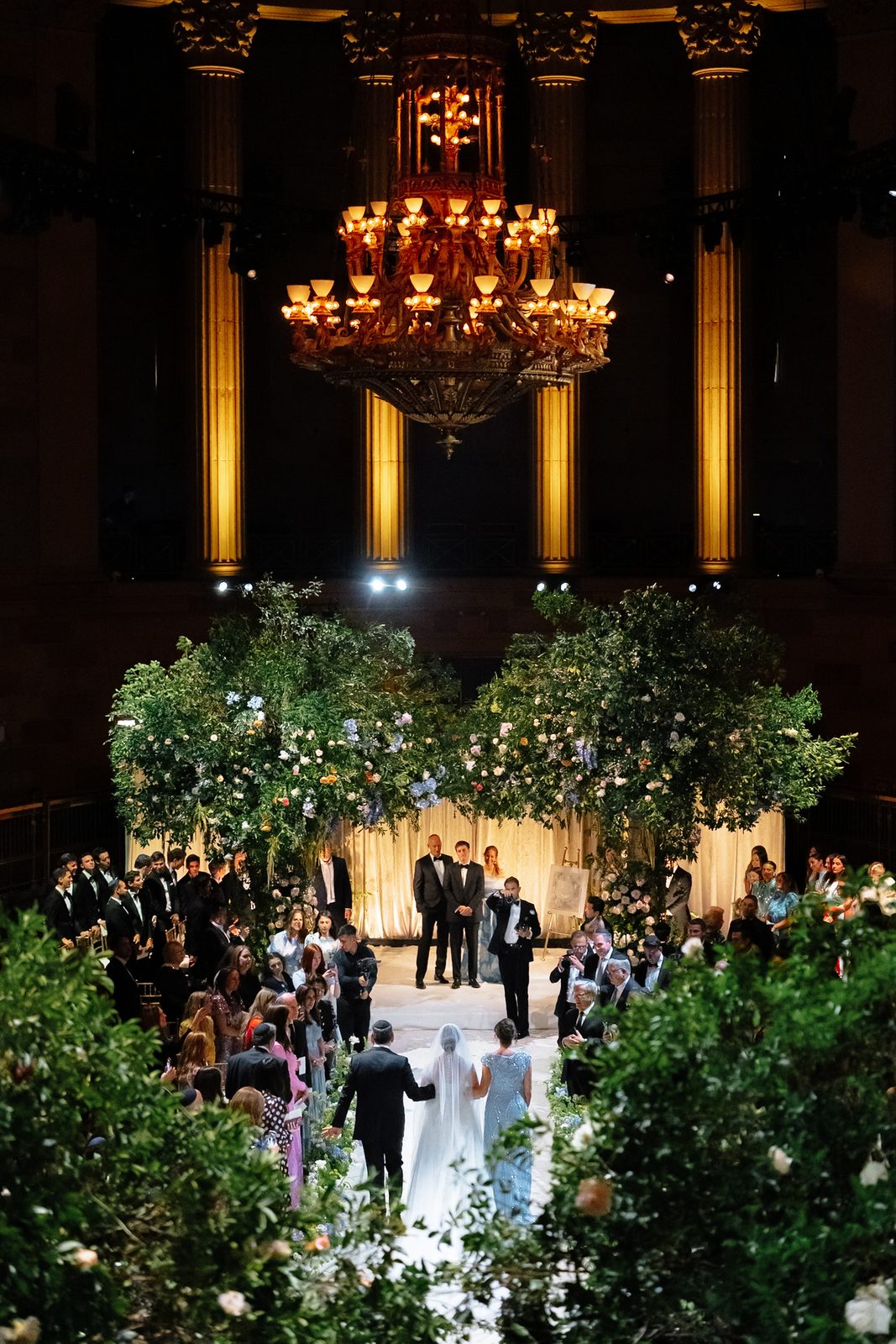 A wide view of the ceremony at Gotham Hall, guests filling the ballroom under the chandelier