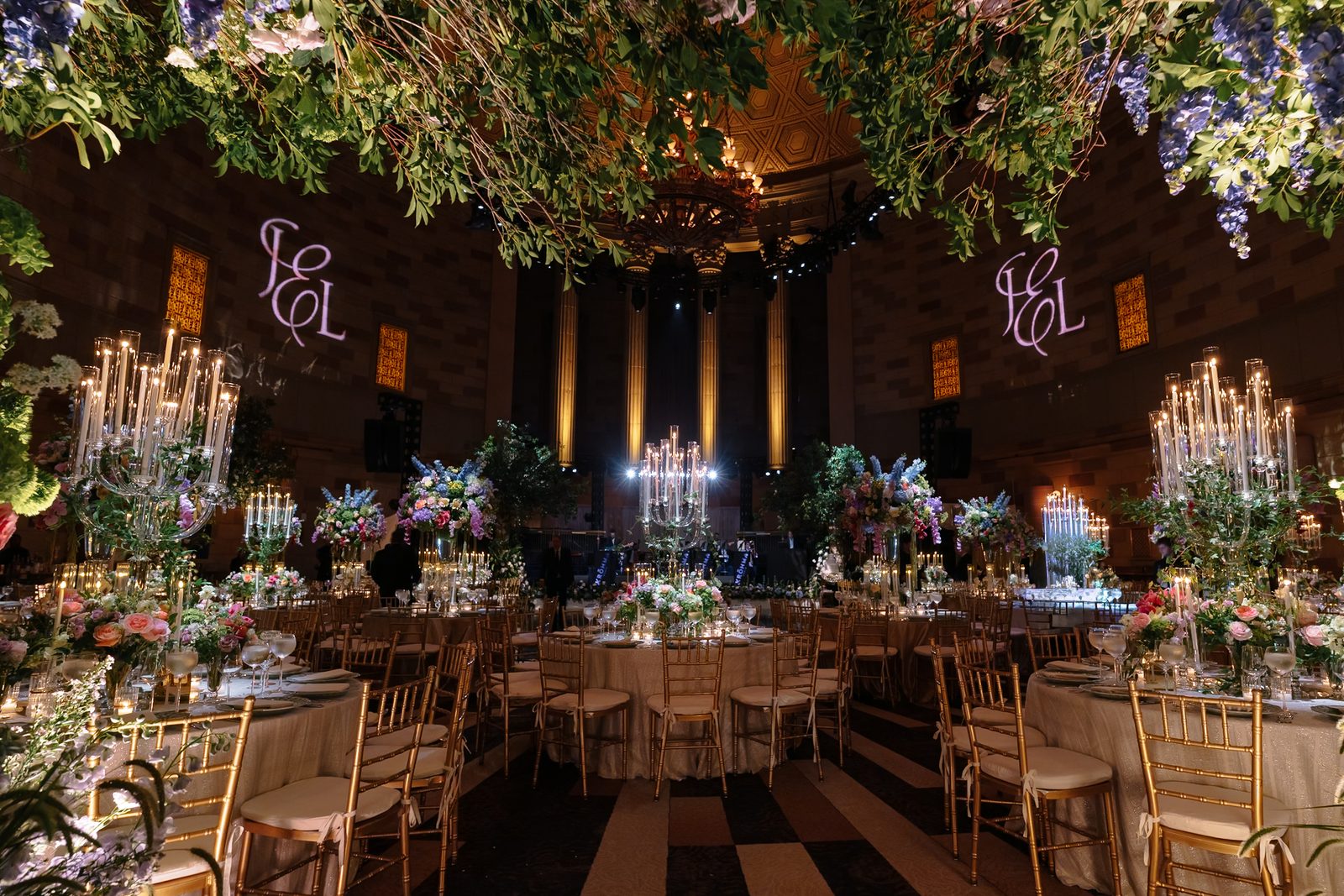 The Gotham Hall ballroom set for dinner, the couple's monogram lit on the wall above the tables