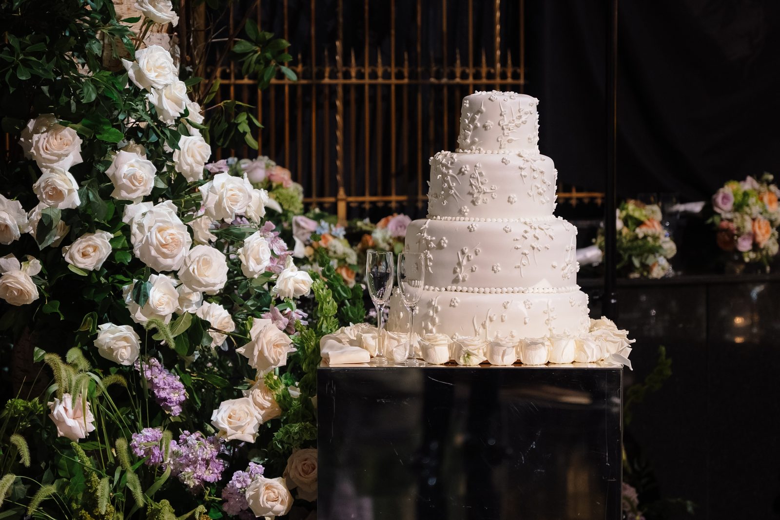 A tiered white wedding cake beside a cascade of garden roses at Gotham Hall