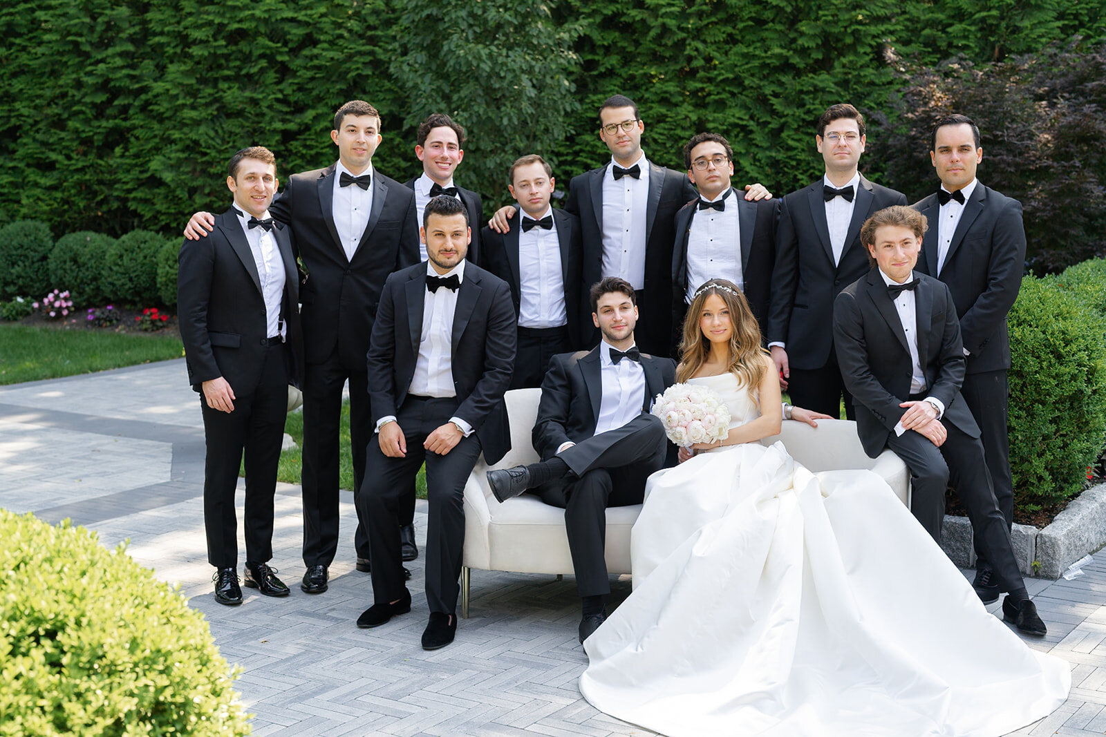The bridal party gathers around Noa and Nate on a garden bench