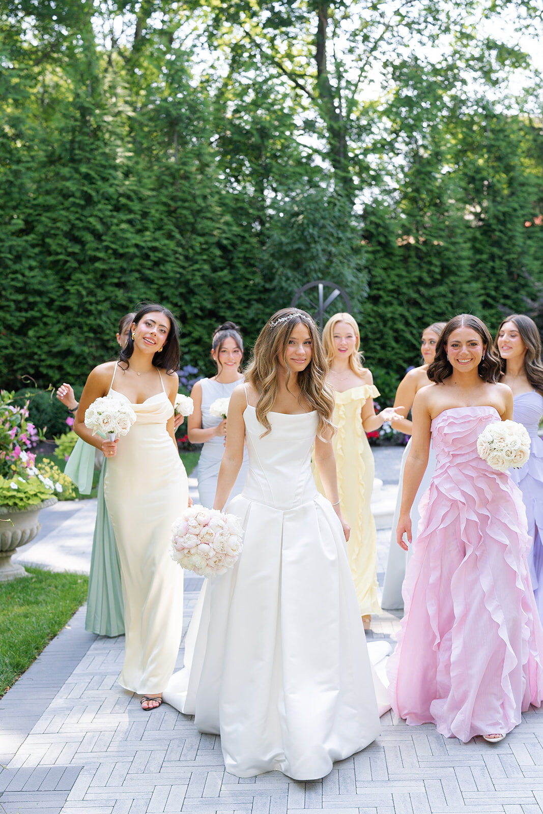 Noa walks the garden path with her bridesmaids in blush, lilac and yellow