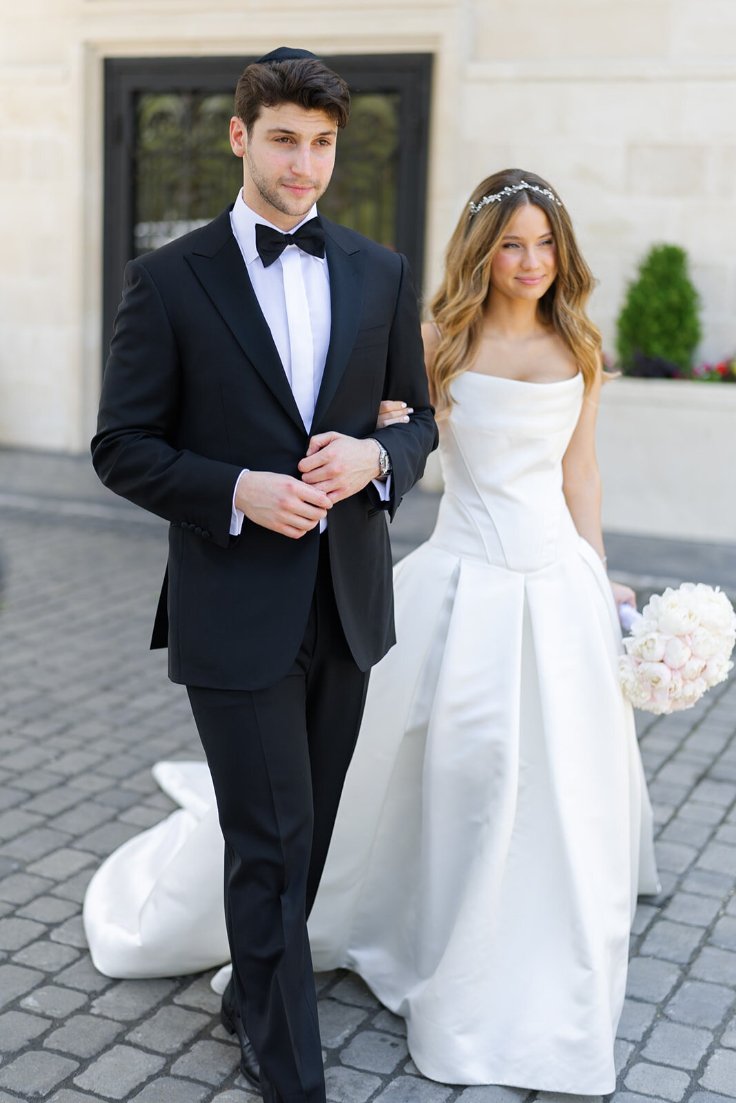 Noa and Nate walk across the stone courtyard in front of the estate