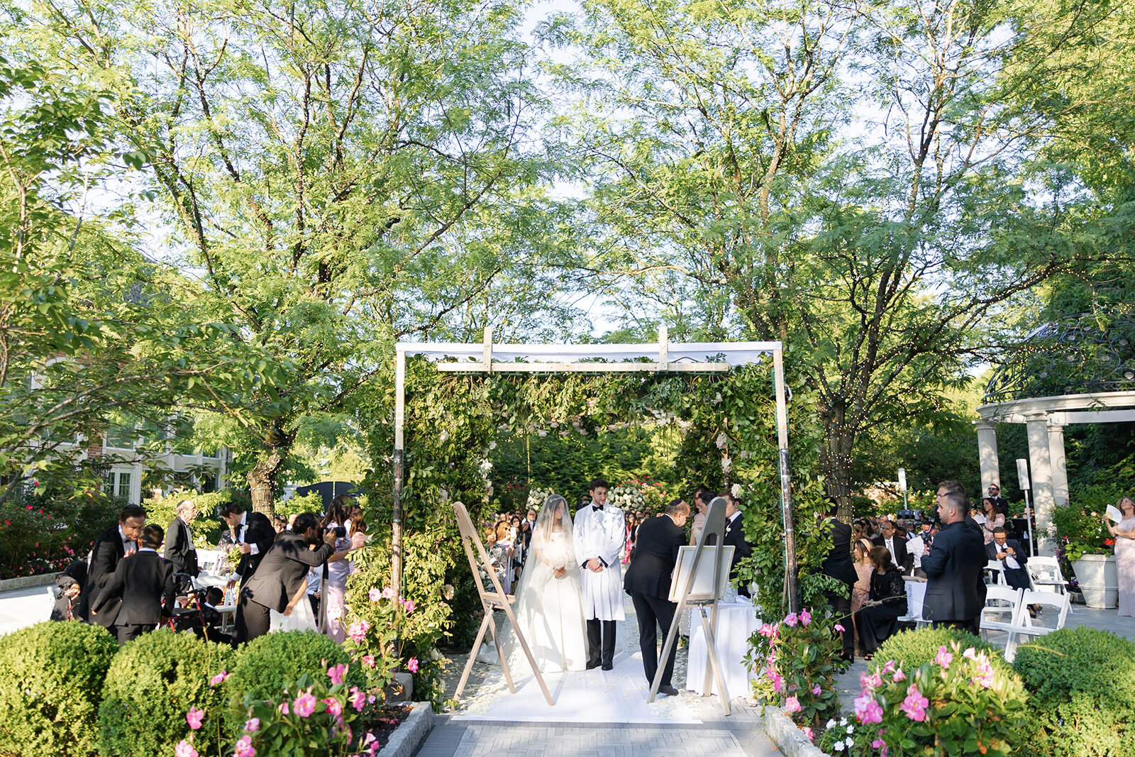 The garden chuppah seen from the back of the ceremony, guests seated under the trees