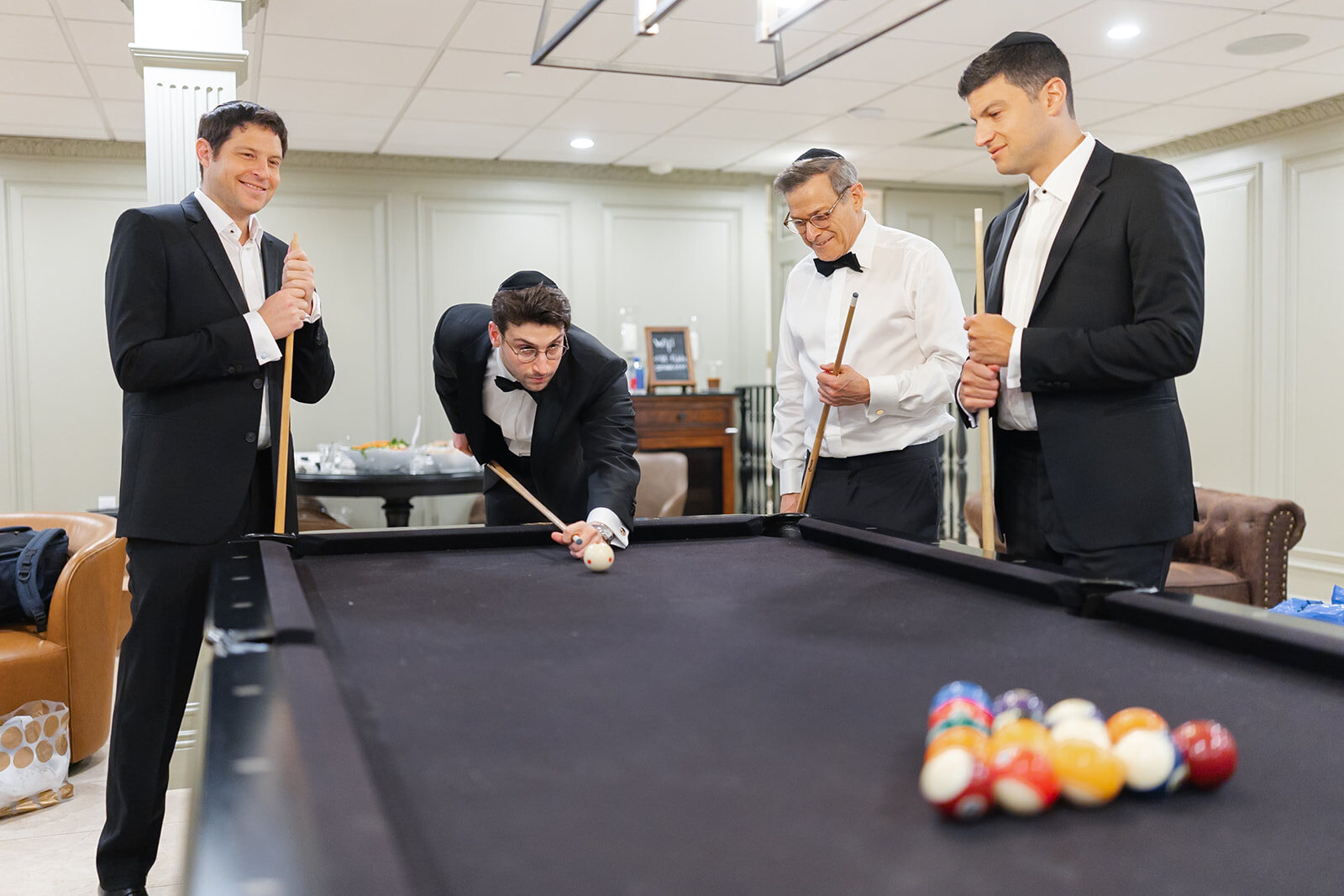 Nate and his groomsmen play pool in their tuxedos before the ceremony