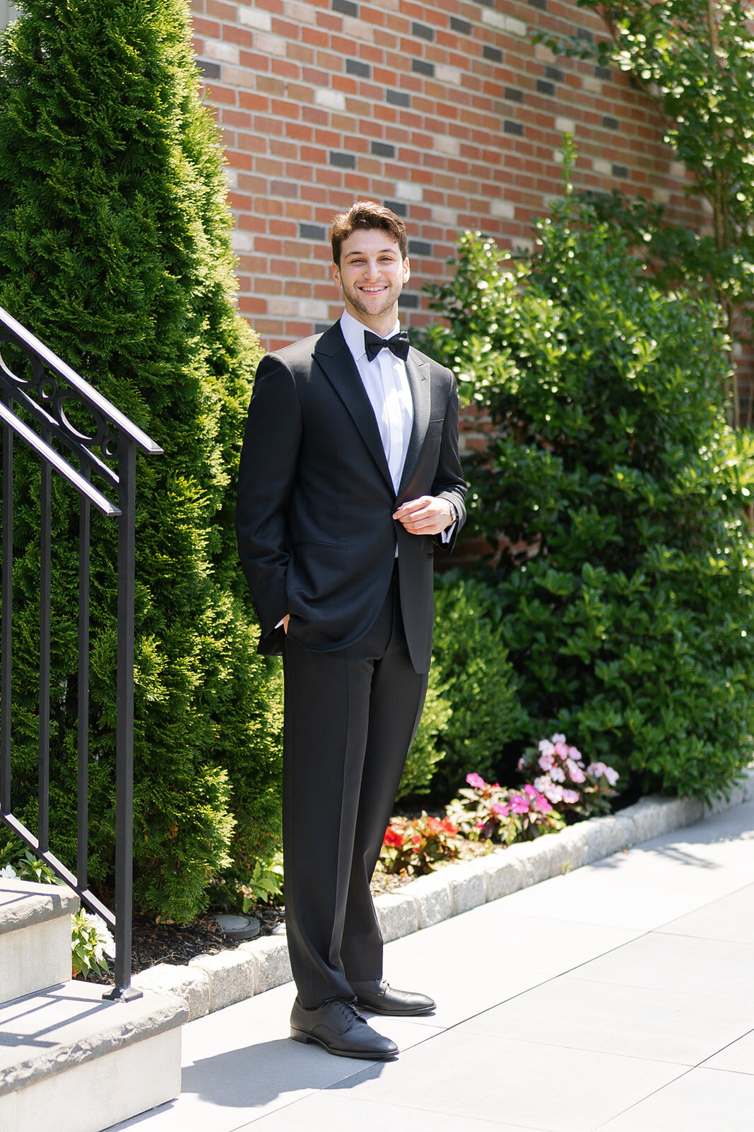 Nate in a black tuxedo on the garden stairs beside the brick wall of the estate