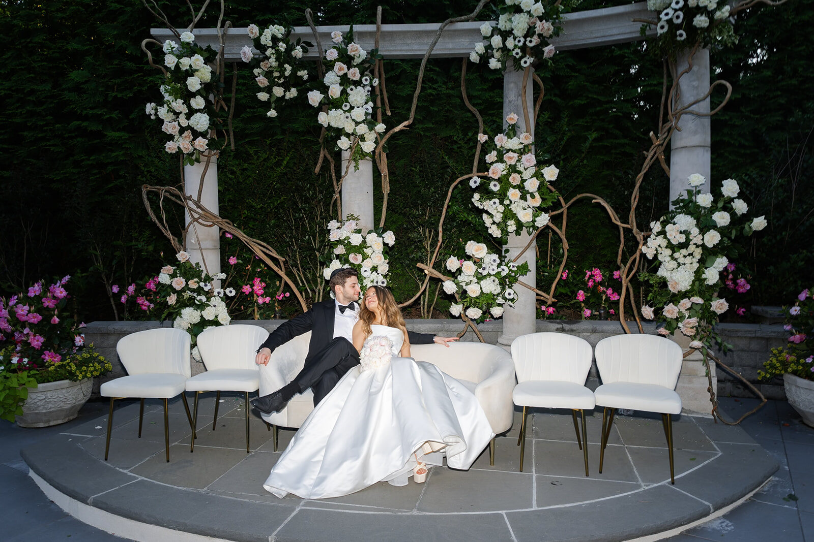 Noa lounges on the white ceremony seating beneath the floral arches
