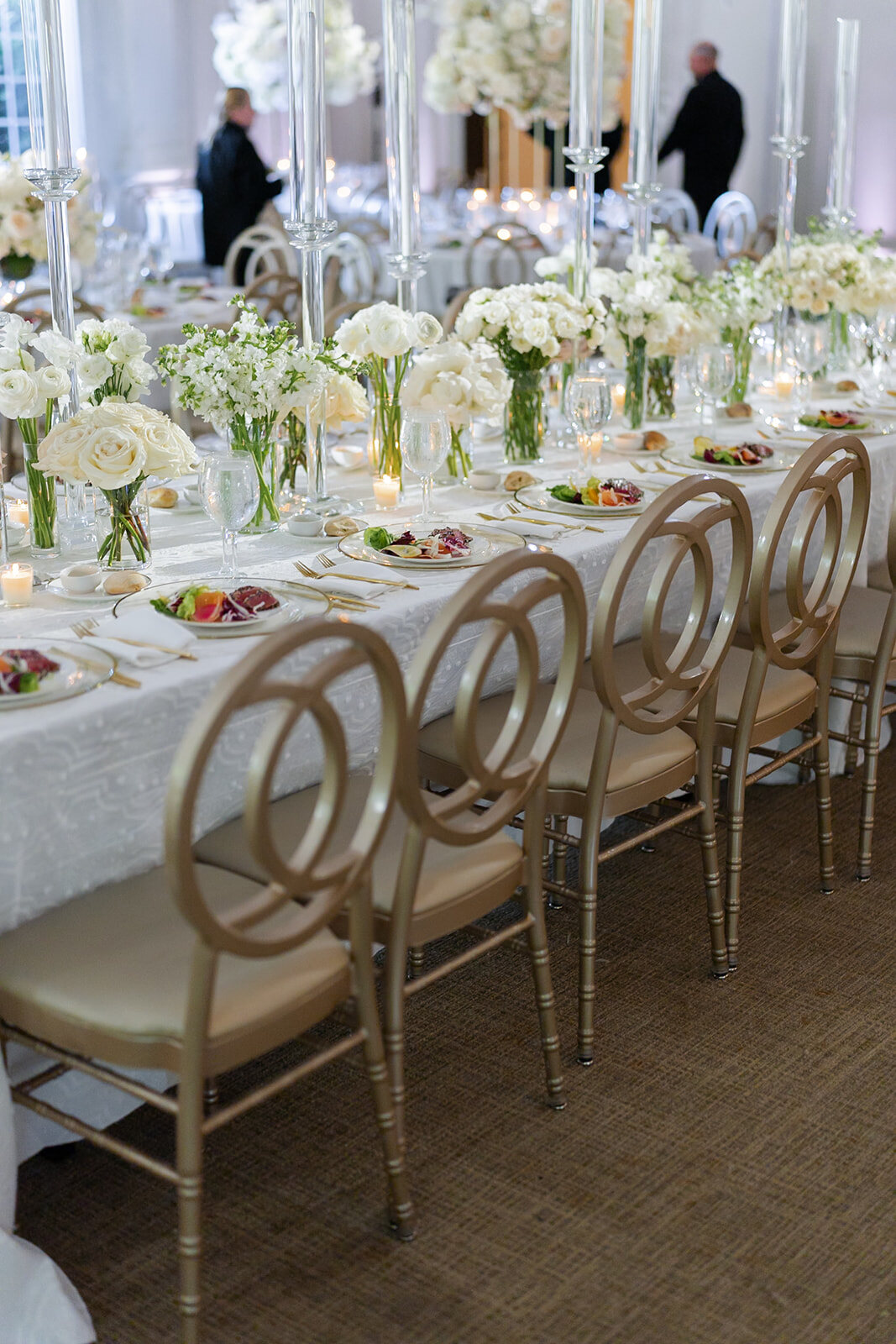 A long reception table set with white florals, candles and gold chairs