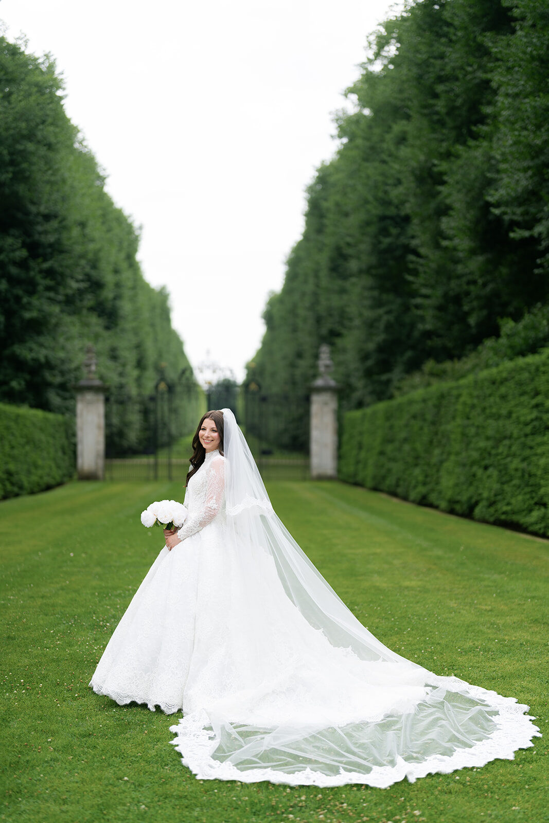 Arielle on a long hedge-lined garden allee, her veil trailing across the grass