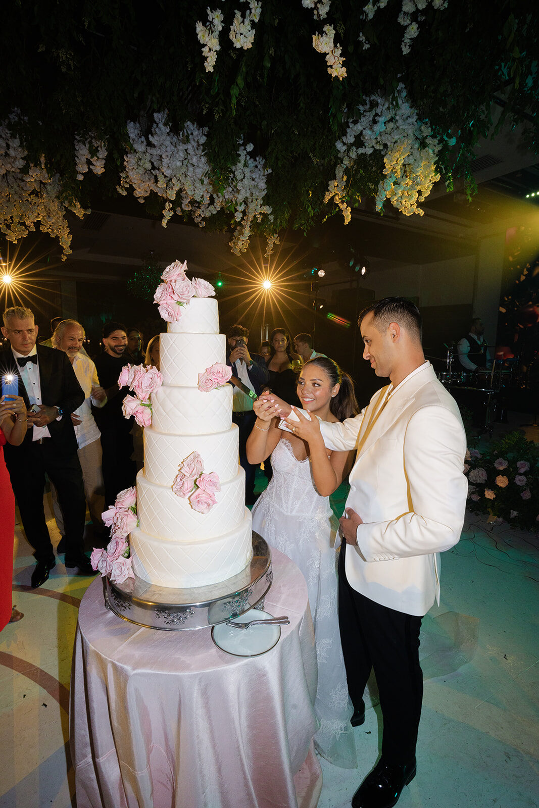 Ashley and Ben cutting a tiered cake with pink roses at Old Westbury Hebrew Congregation