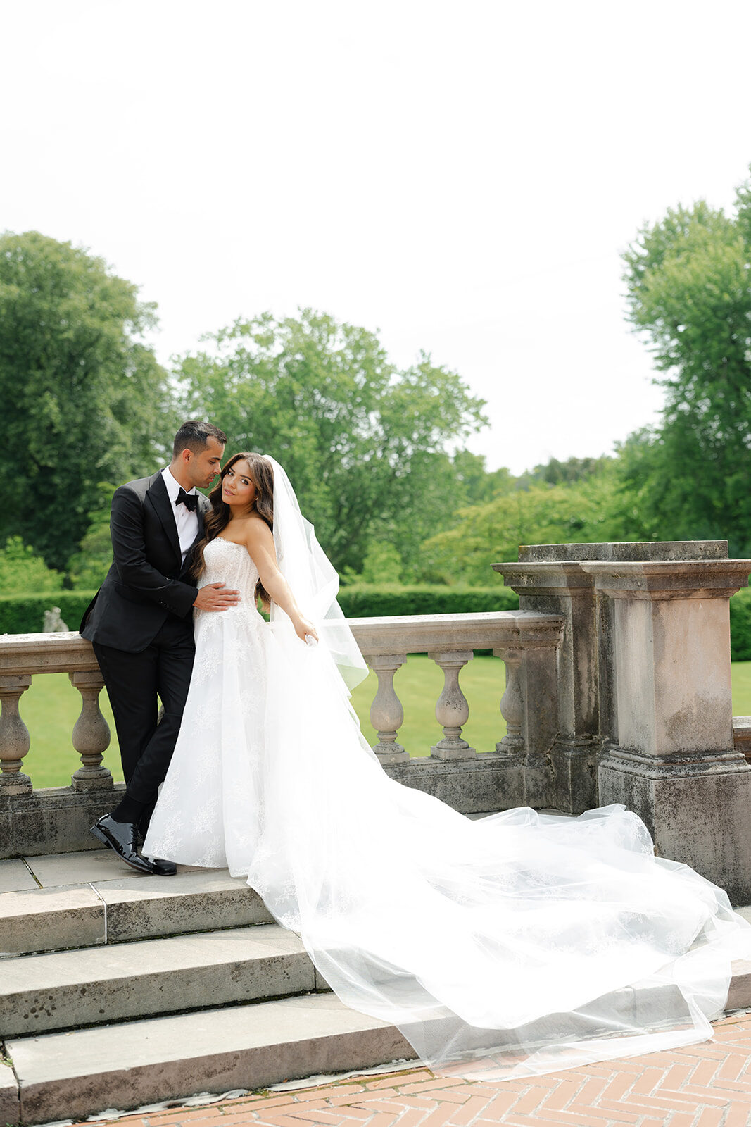 Ashley and Ben on a stone balustrade above the lawn, her train spilling down the steps