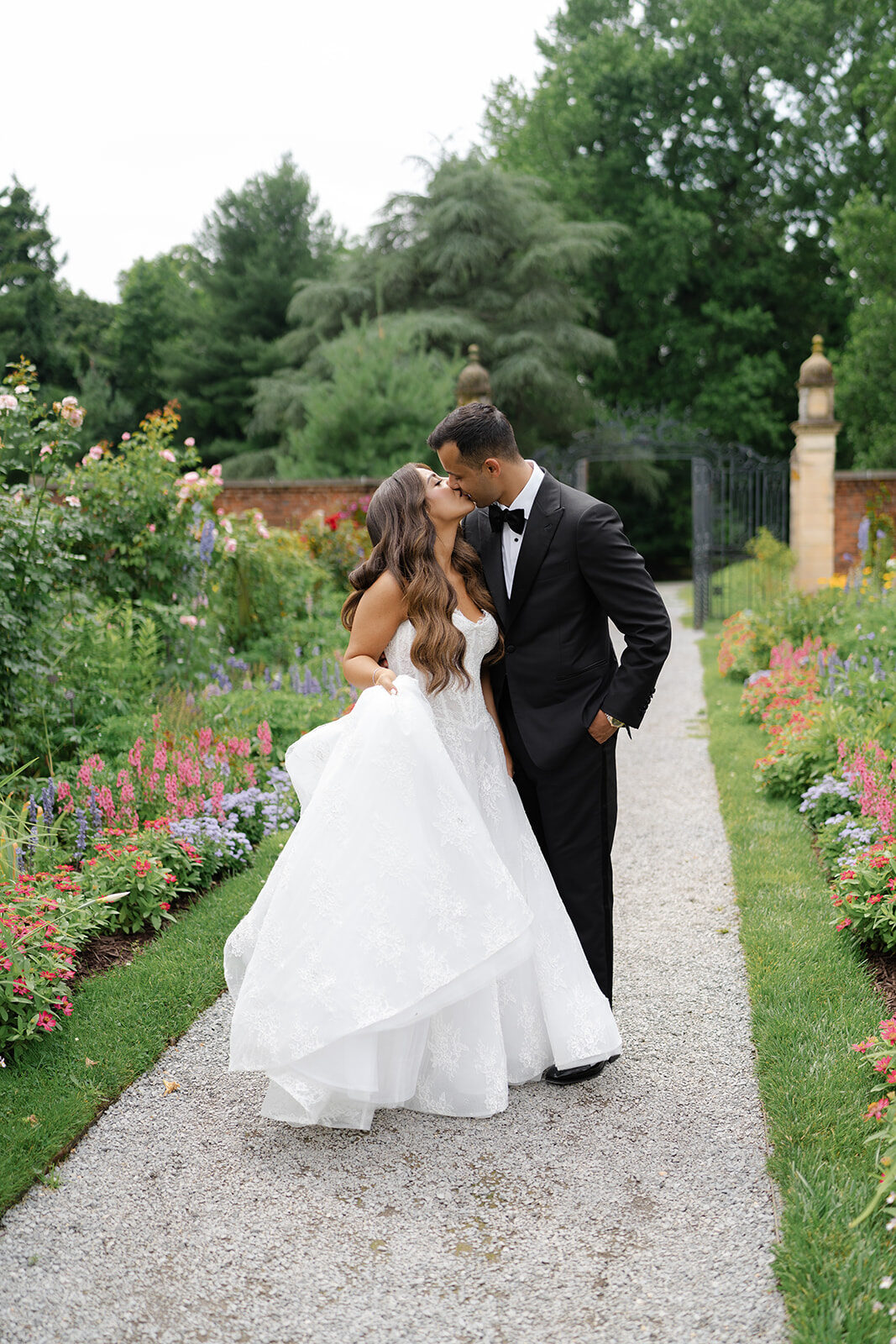Ashley and Ben walking a garden path lined with roses during portraits near Old Westbury