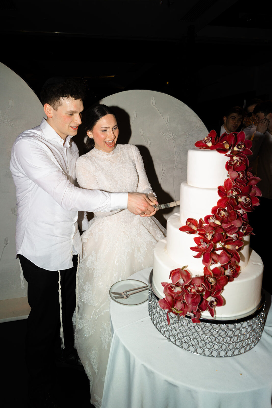 Kelly and Jacob cutting a white cake wrapped in red roses at Old Westbury Hebrew Congregation