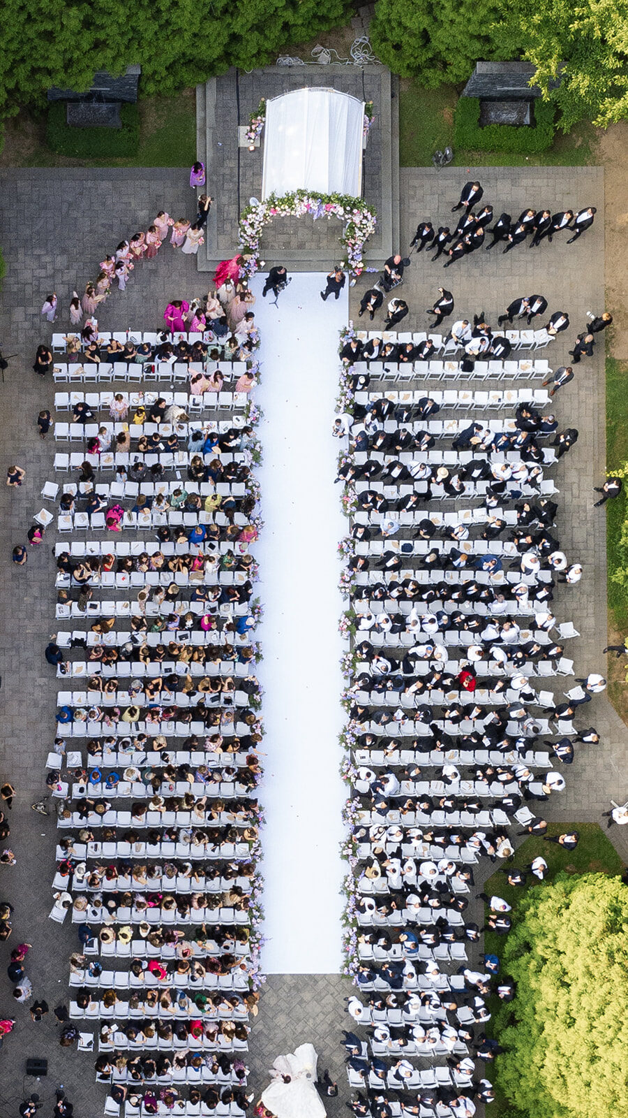 Aerial view of an outdoor wedding ceremony at Old Westbury Hebrew Congregation, hundreds of guests either side of a white aisle