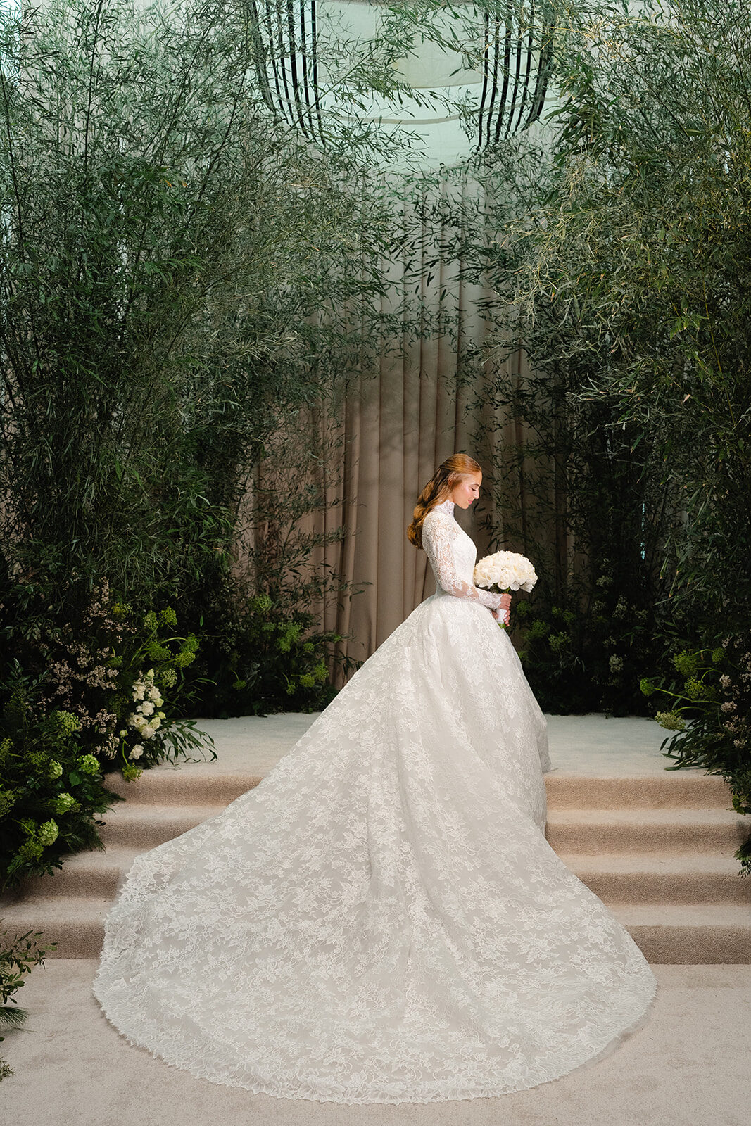 Rebecca in a lace gown on the steps of the greenery archway inside Old Westbury Hebrew Congregation