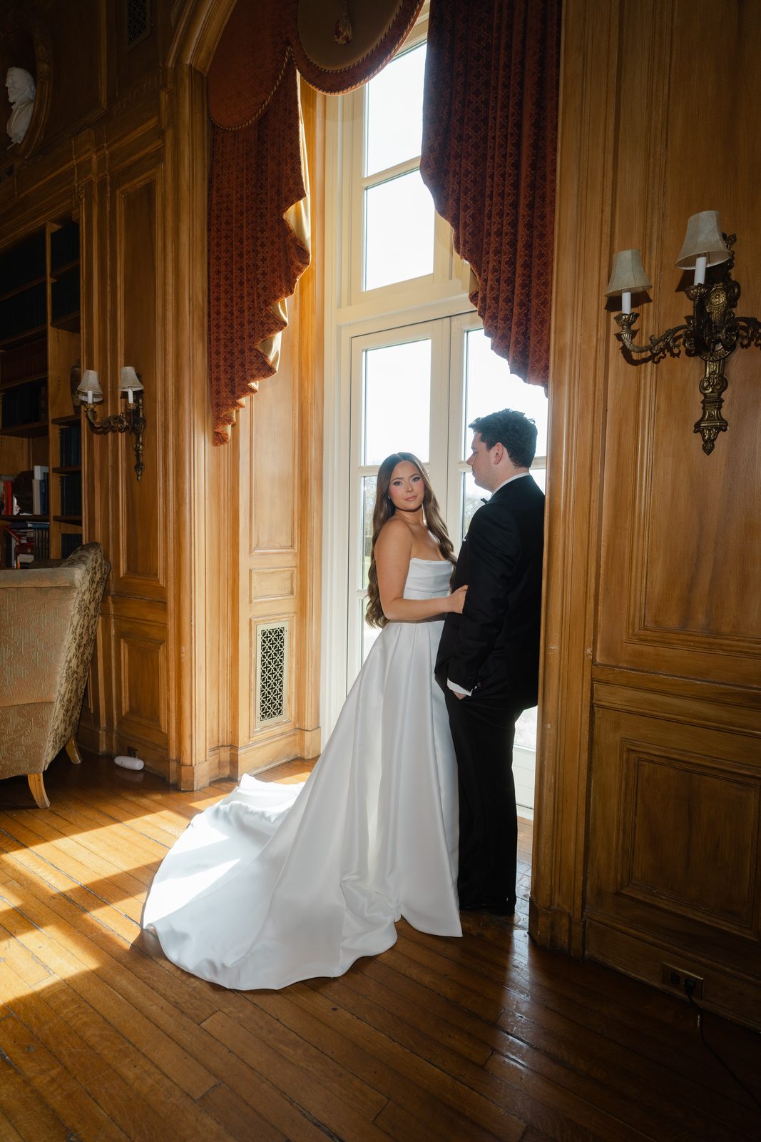 Rachel and Ian by the tall windows in a wood-panelled room at Oheka Castle