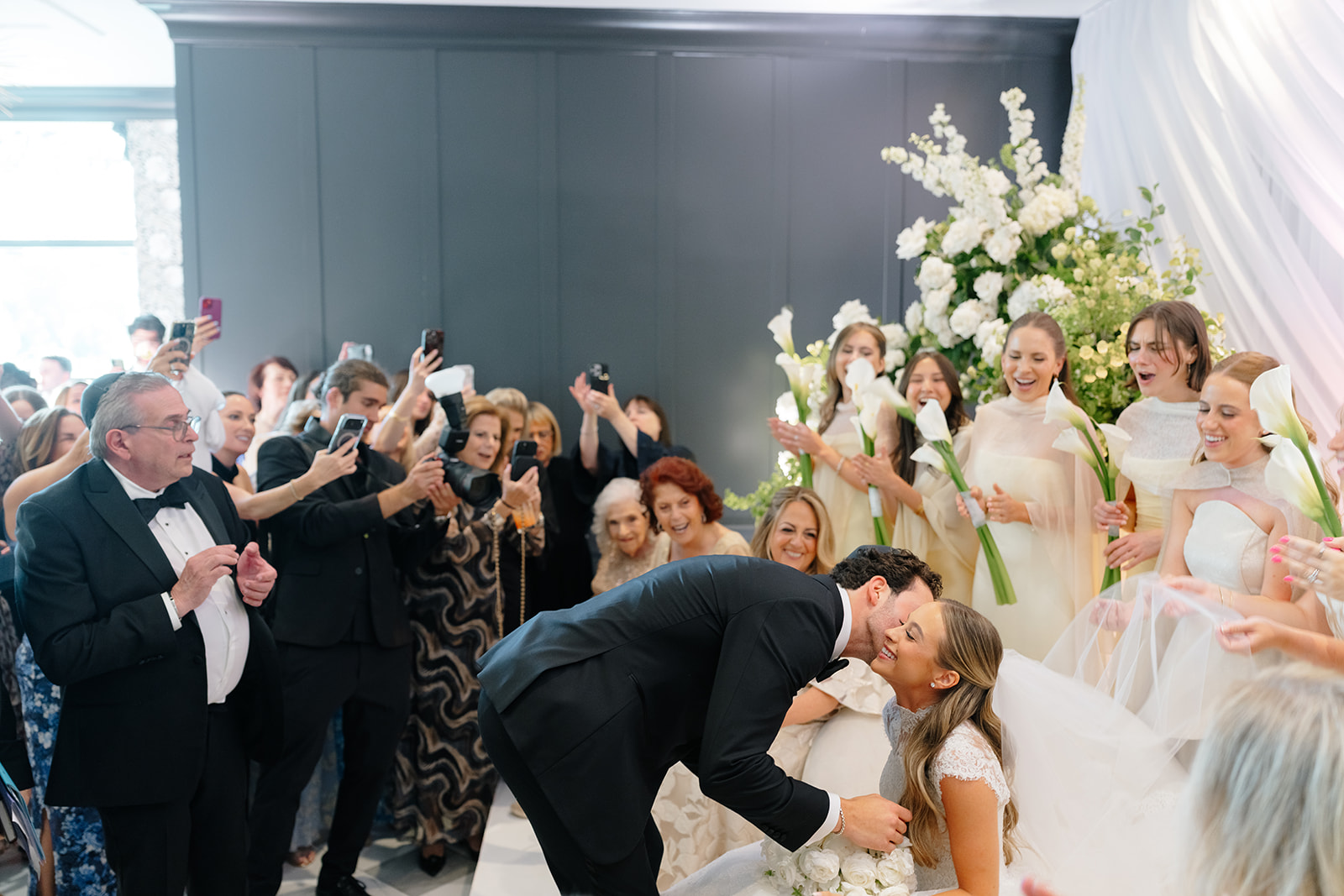Phil lowers the veil over Rebecca at the bedeken as bridesmaids holding calla lilies look on