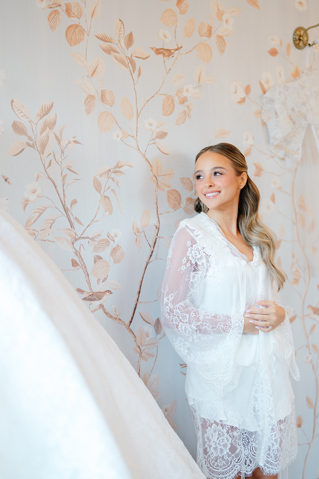 Rebecca in a lace robe in the bridal suite, her gown hanging against chinoiserie wallpaper