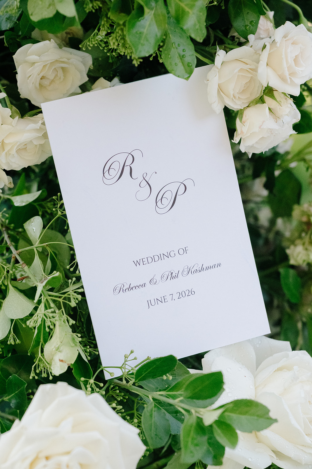 The wedding program for Rebecca and Phil, nestled in white roses and greenery
